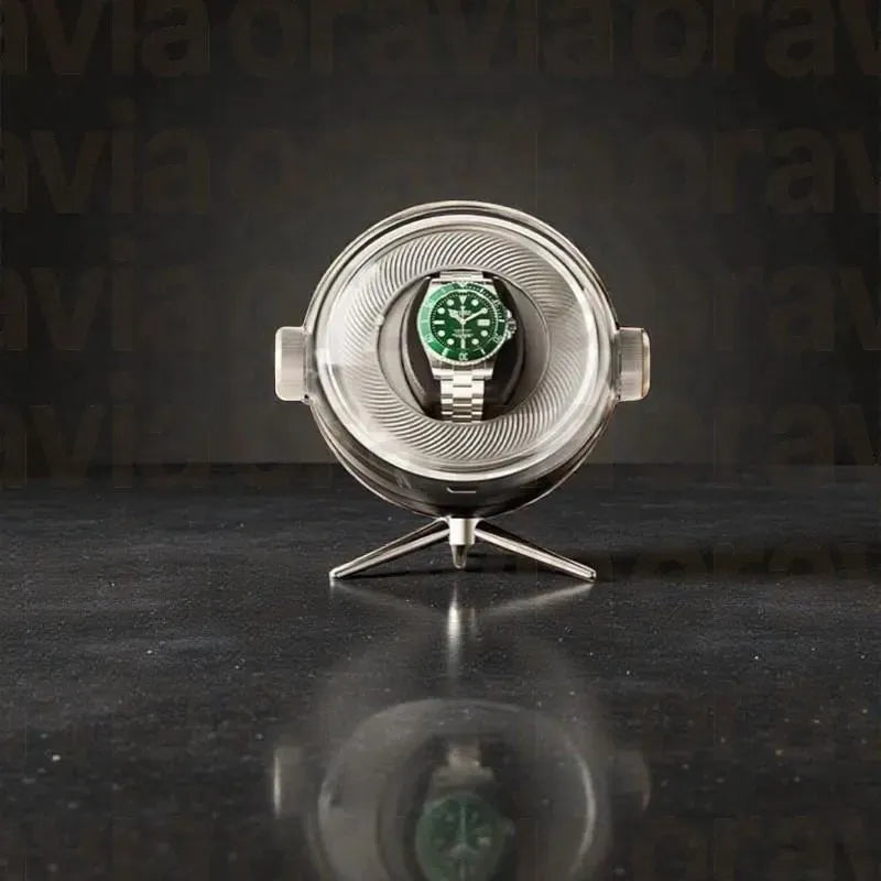 Silver watch display case with a green watch inside on a dark reflective surface.