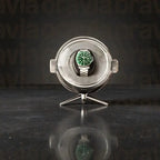 Silver watch display case with a green watch inside on a dark reflective surface.