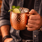 Copper mug with a cocktail garnished with lime and mint, held by a person.