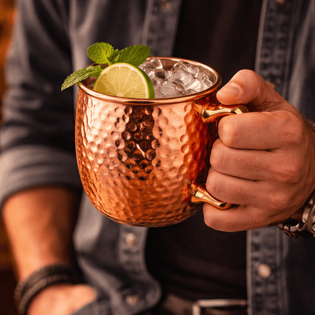 Copper mug with a cocktail garnished with lime and mint, held by a person.