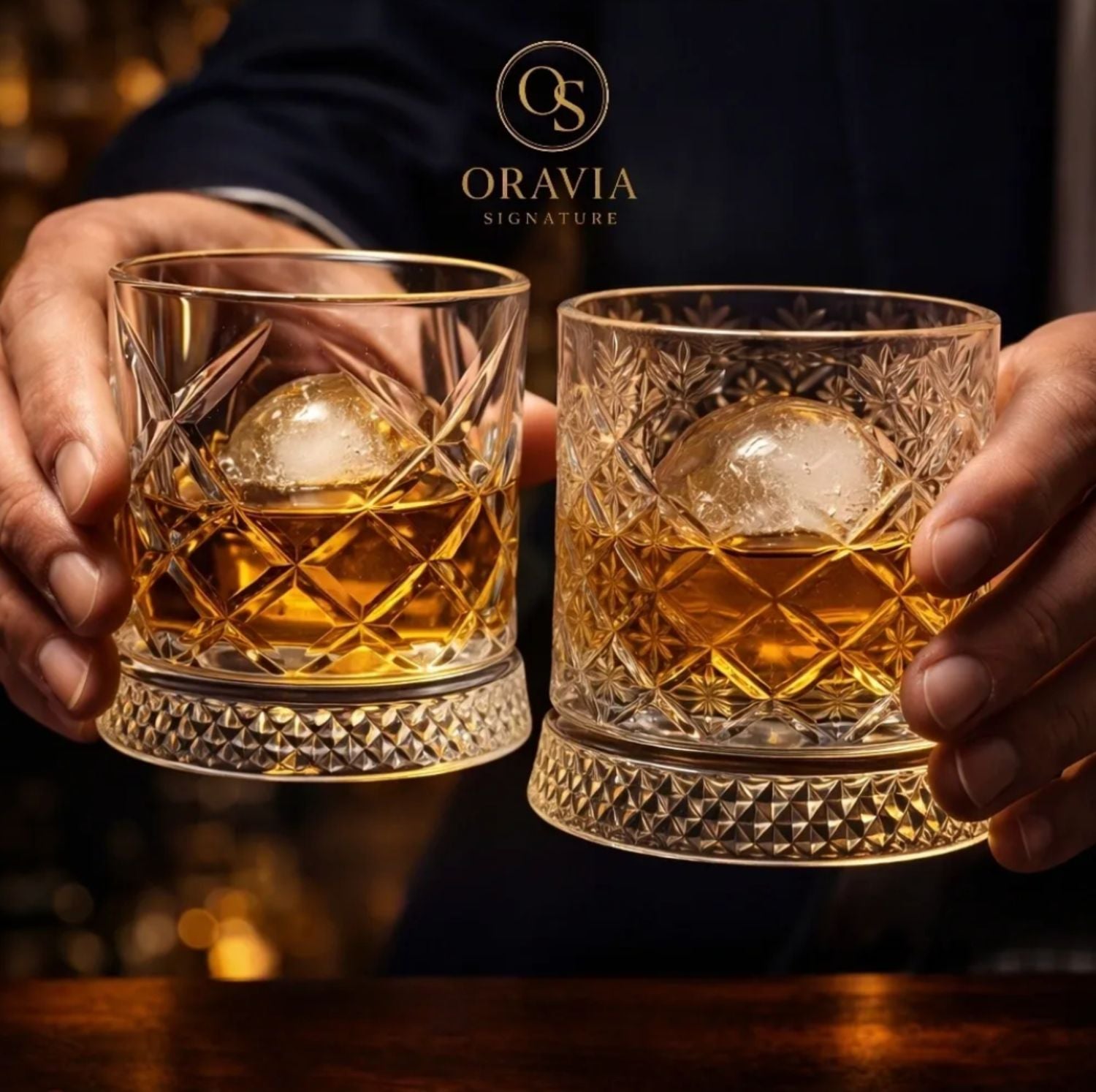 Two hands holding crystal glasses filled with a golden liquid and ice cubes, with Oravia Signature logo in the background.