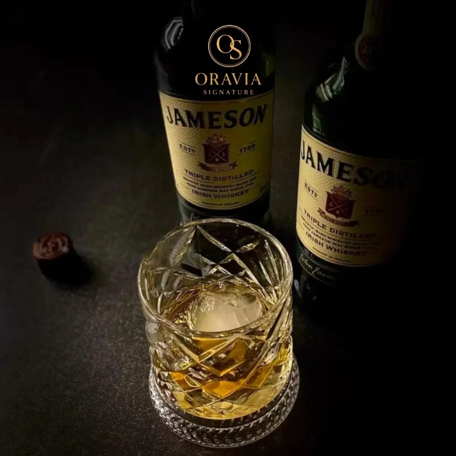 Two bottles of Jameson whiskey with a glass filled with whiskey on a dark surface.