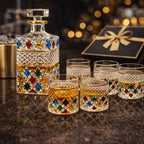 Decorative whiskey decanter and glasses with gemstone accents on a dark surface.