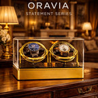 Two watches in a gold and clear display case with 'ORAVIA' branding in an elegant room.