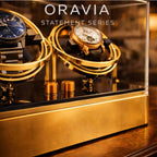 Two watches in gold cases on a reflective surface with 'ORAVIA' branding.