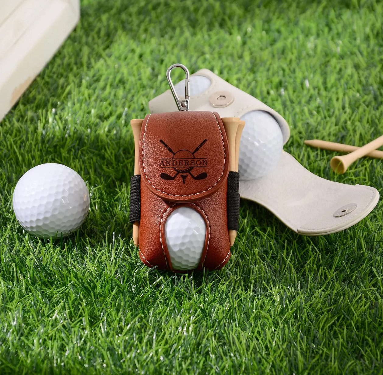 Golf ball in a leather holder on grass with golf club and balls in the background