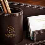 Brown leather pen holder with 'Oravia Signature' branding on a wooden surface.