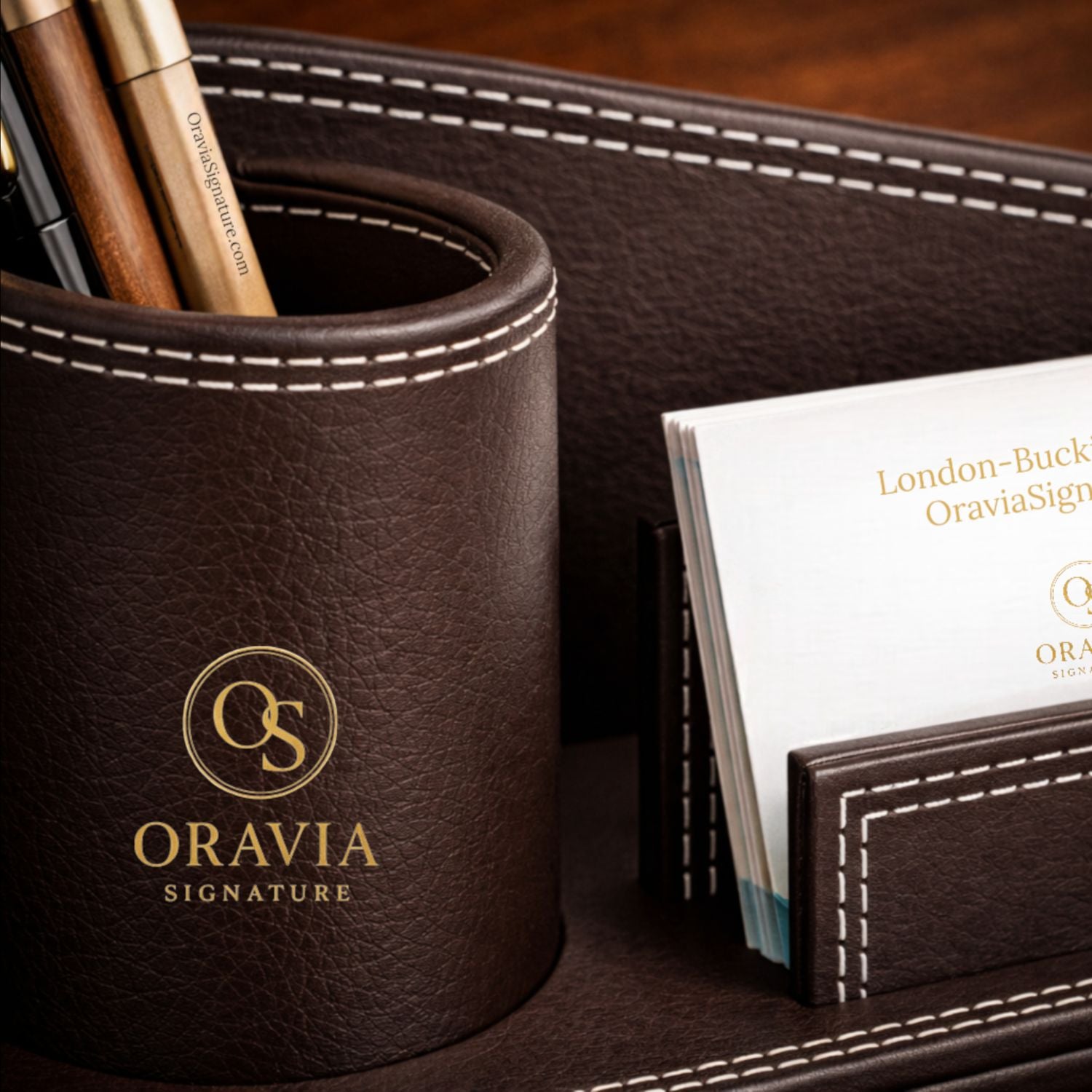 Brown leather pen holder with 'Oravia Signature' branding on a wooden surface.