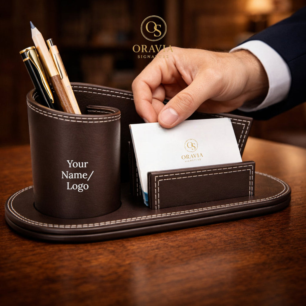 Brown leather desk organizer with pen holder and card holder on a wooden surface, featuring the Oravia Signature logo.