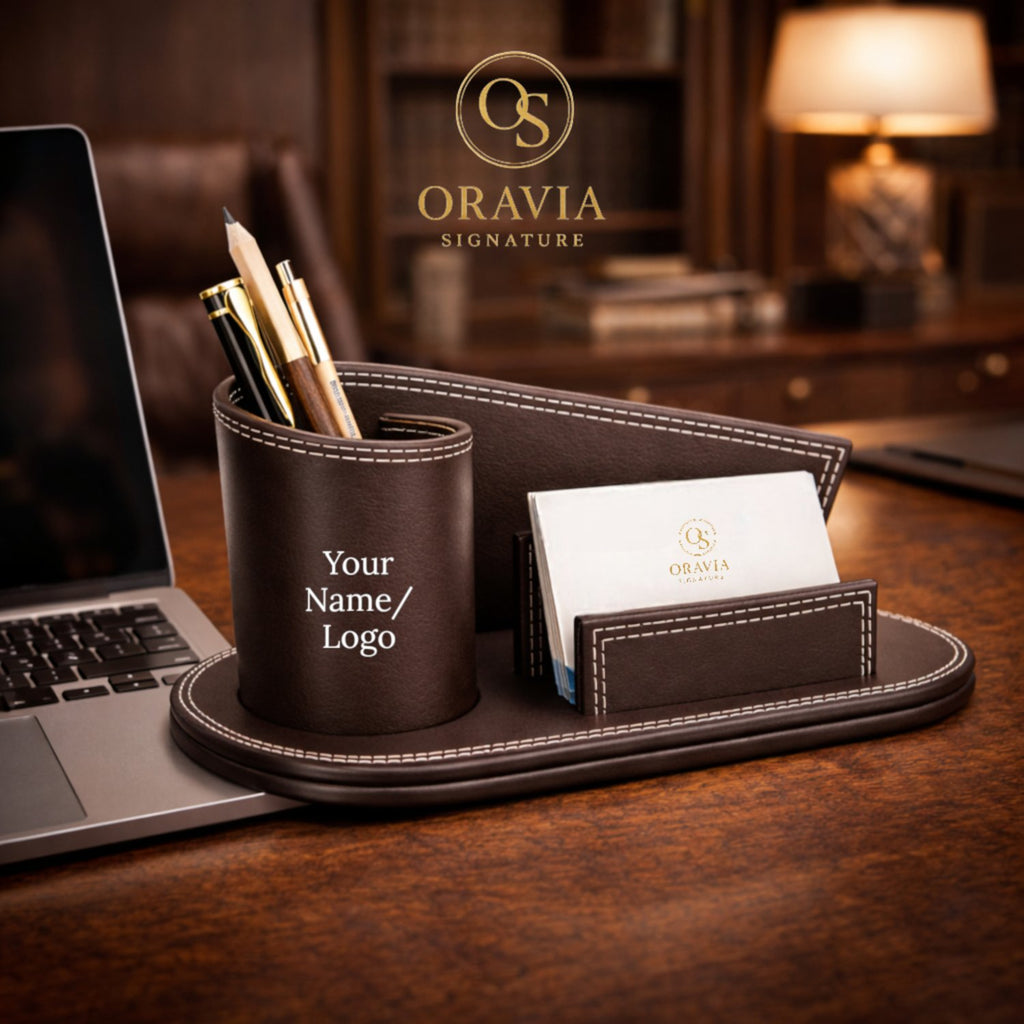 Brown leather desk organizer with pen holder, card holder, and laptop on a wooden desk with 'Oravia' branding.