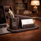 Brown leather desk organizer with pen holder, card holder, and laptop on a wooden desk with 'Oravia' branding.