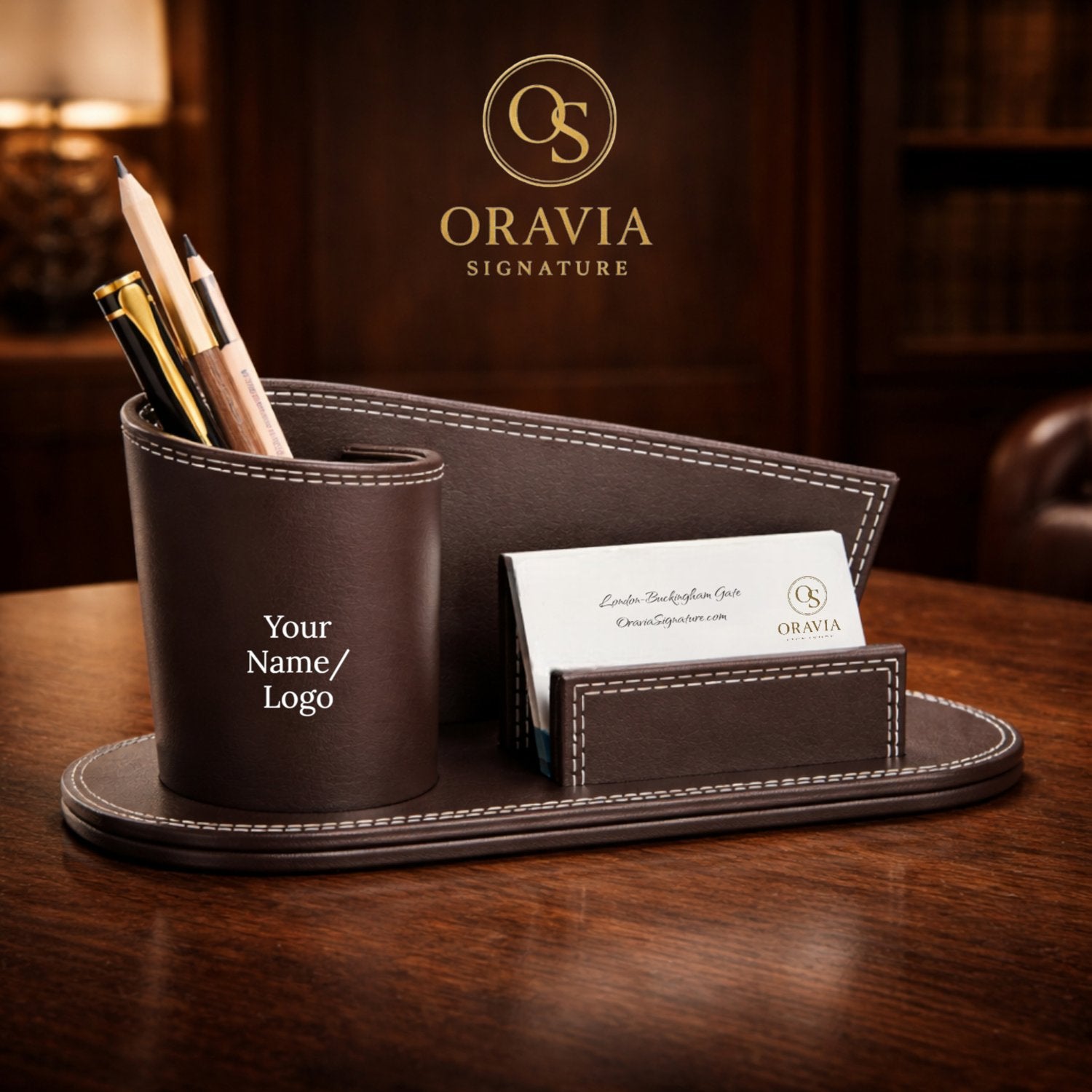 Brown leather desk organizer with pens and a card on a wooden surface, featuring the Oravia Signature logo.