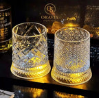Two ornate glass tumblers on a reflective surface with 'Oravia' branding in the background.