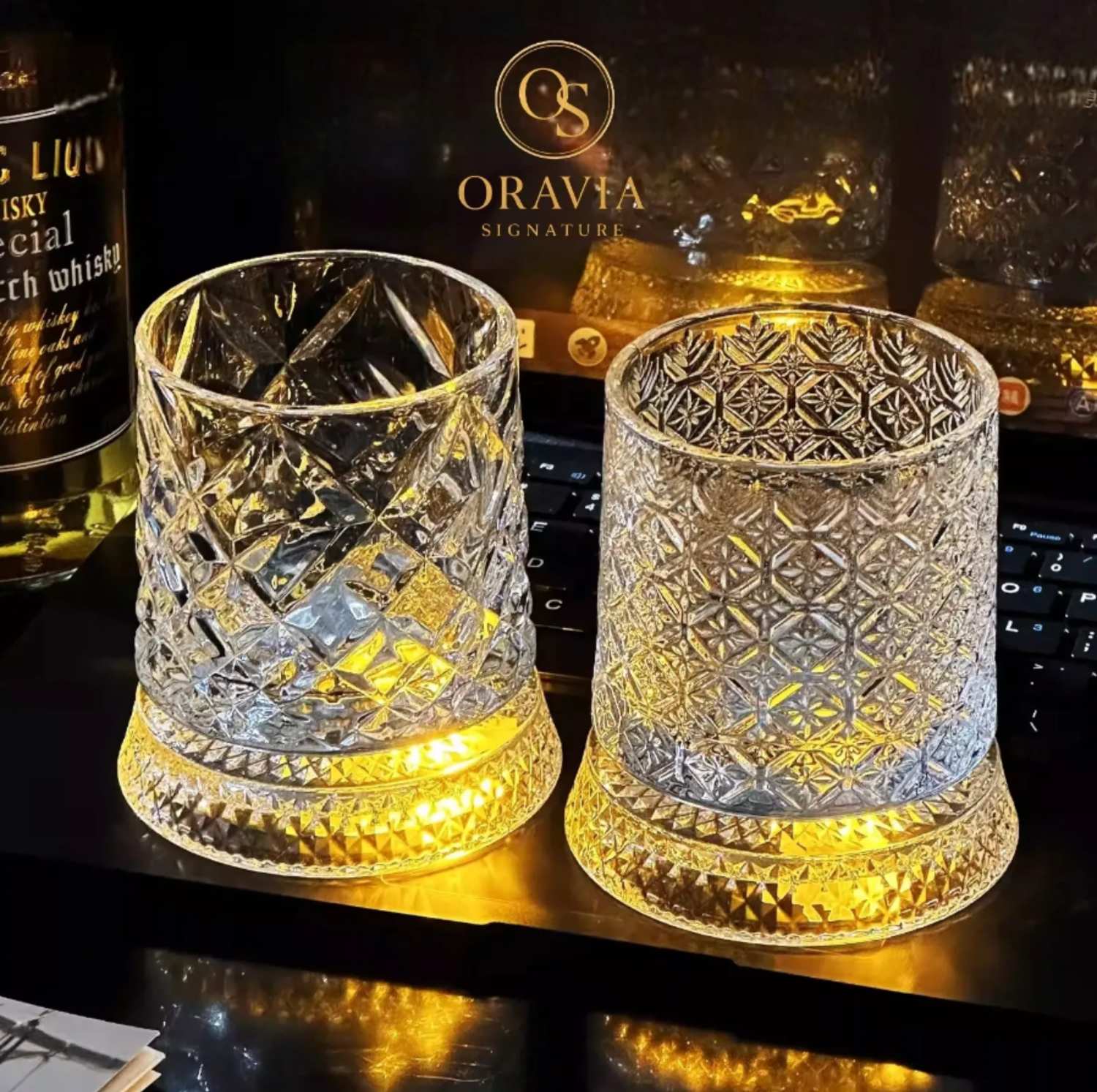 Two ornate glass tumblers on a reflective surface with 'Oravia' branding in the background.