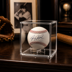 Signed baseball in a clear display case on a wooden surface with a baseball glove and bat in the background.
