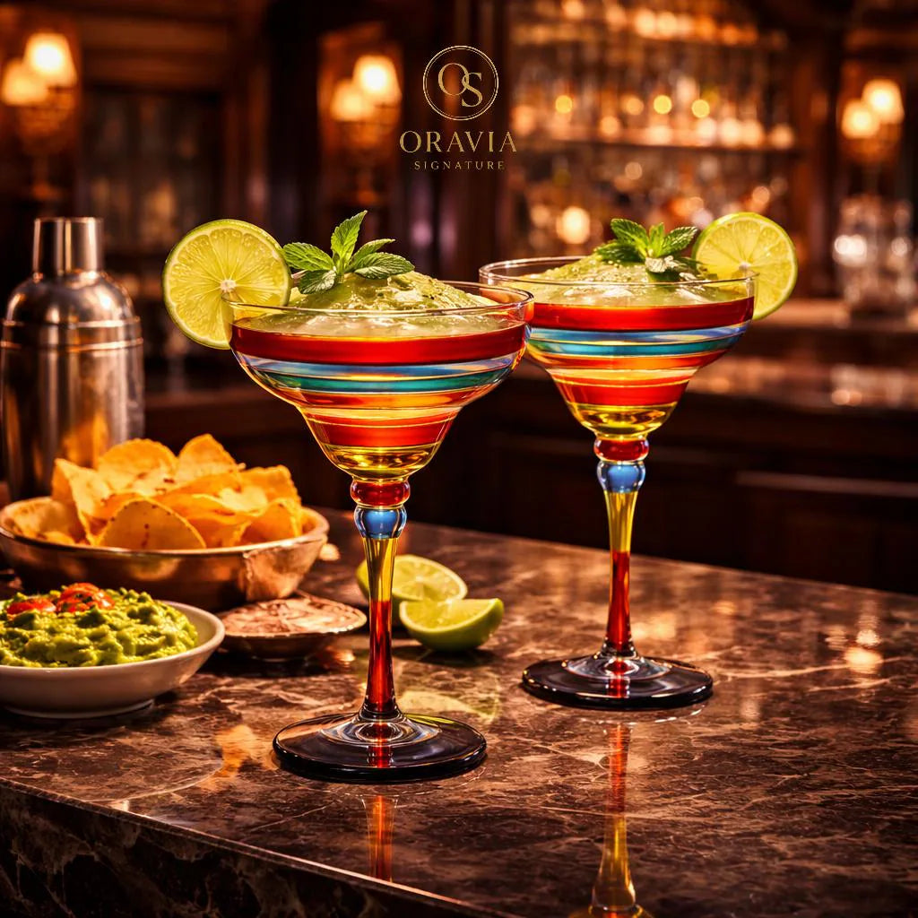 Two colorful margarita glasses with lime wedges on a bar counter, featuring Oravia Signature branding.