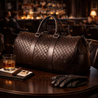 Brown leather duffel bag on a table with a glass of whiskey, a cigar, and gloves in a bar setting.
