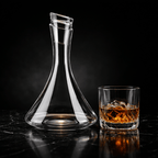 Clear glass decanter and whiskey glass with ice on a dark surface