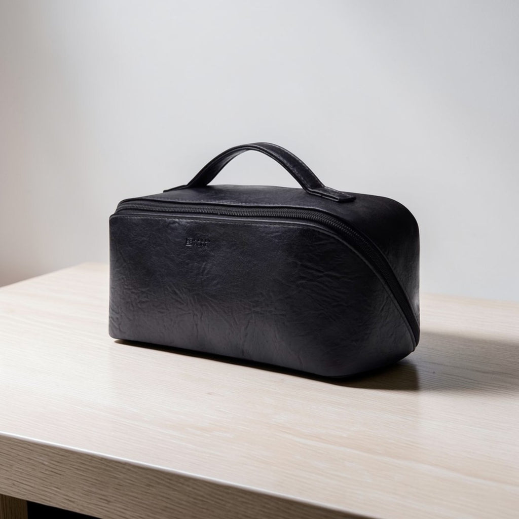Black leather toiletry bag on a light wooden surface with a neutral background