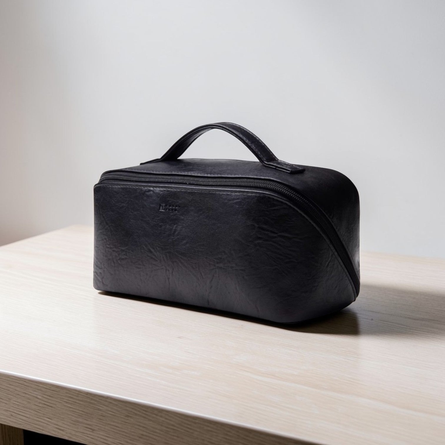 Black leather toiletry bag on a light wooden surface with a neutral background