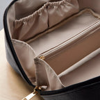 Open beige toiletry bag with black zipper on a light wooden surface