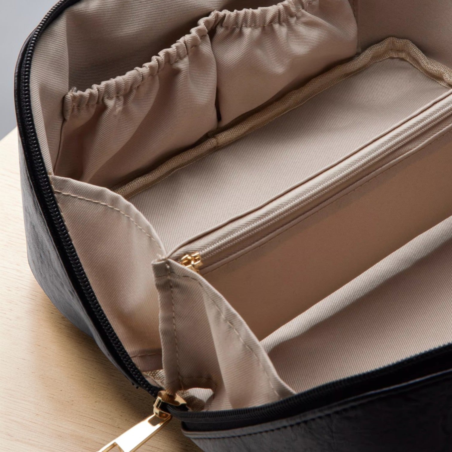 Open beige toiletry bag with black zipper on a light wooden surface