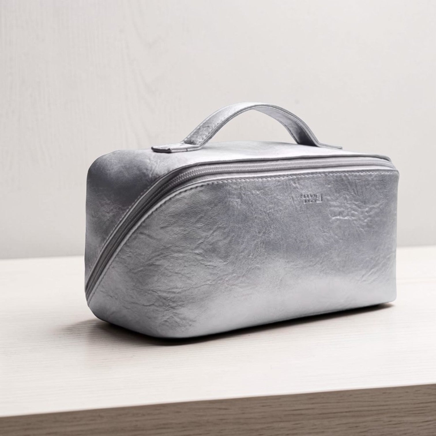 Silver toiletry bag on a light wooden surface with a neutral background