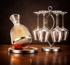 Decorative glass decanter with a stand and hanging wine glasses on a wooden surface.