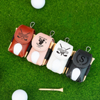Four personalized golf club head covers on a green surface with golf balls and tees.