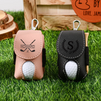 Two golf ball holders with golf balls inside on grass, one pink and one black, with visible branding.
