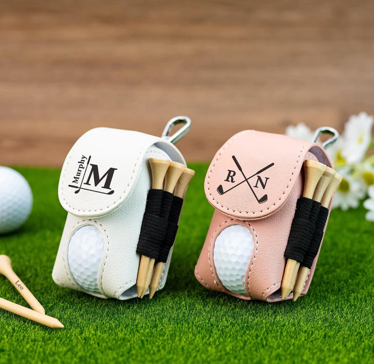 Two golf ball and tee sets in personalized cases on a grassy surface with a wooden background.