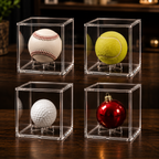 Four clear display cases with baseball, tennis ball, golf ball, and red ornament on a wooden surface.