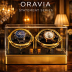 Two watches in a gold display case with 'ORAVIA' branding in an elegant room setting.