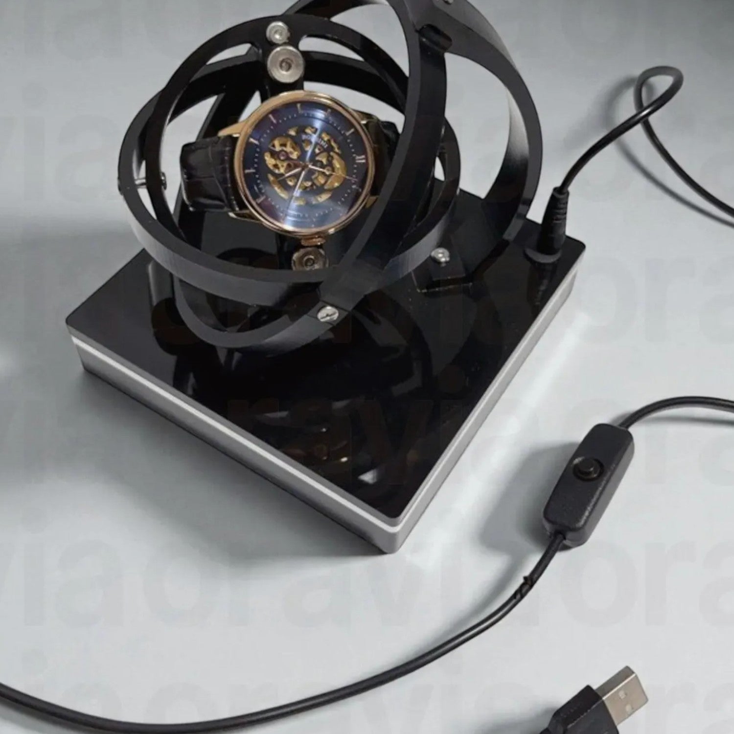 Watch winder  in a black metal stand with USB cable on a light gray background